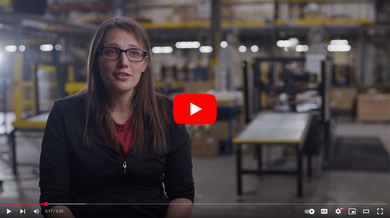 Woman speaking in a warehouse setting, sharing insights about her work experience, with shelves and equipment visible in the background.