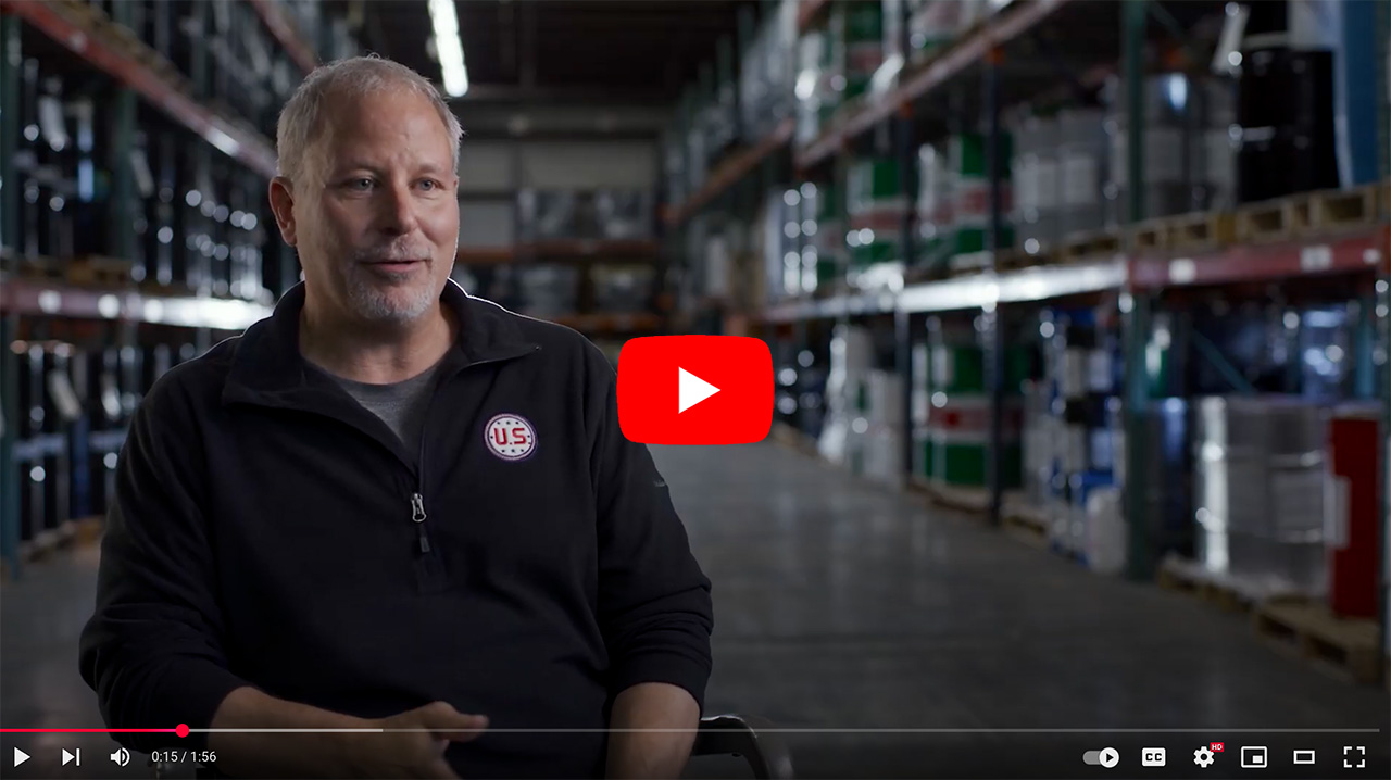 Man speaking in a warehouse setting, surrounded by shelves stocked with industrial containers, discussing his experiences and insights in the industry.