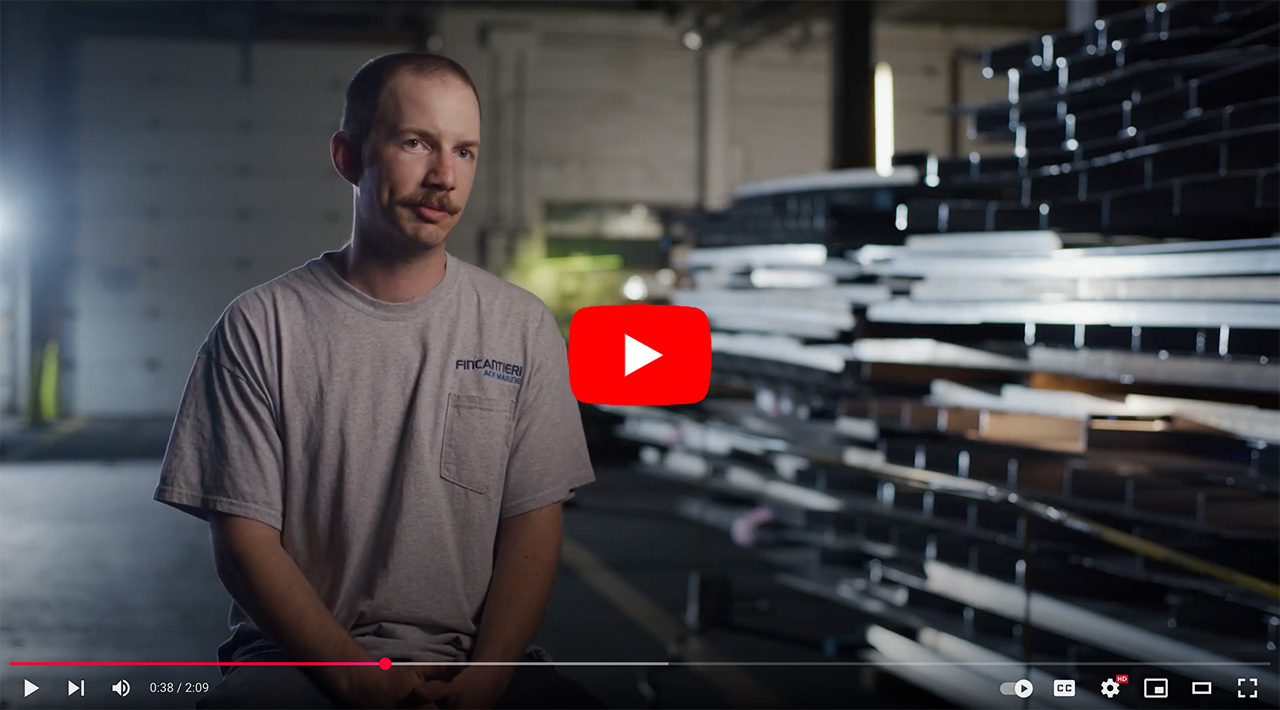 Man sitting in a warehouse, discussing his work experience, with steel plates stacked in the background and a soft light illuminating the scene.