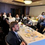 Business professionals attending a formal event in a well-decorated dining room, seated at tables with elegant table settings, engaged in conversation and networking.