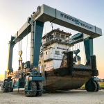 Marine travel lift hoisting a large boat at a shipyard during sunset, showcasing maritime maintenance and repair operations.