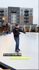 Young man ice skating at The Plaza at Gateway Park, surrounded by modern buildings and festive lights, promoting winter activities and community engagement.