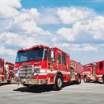 Three red fire trucks parked on a tarmac under a blue sky with fluffy clouds, showcasing their emergency response features and branding.